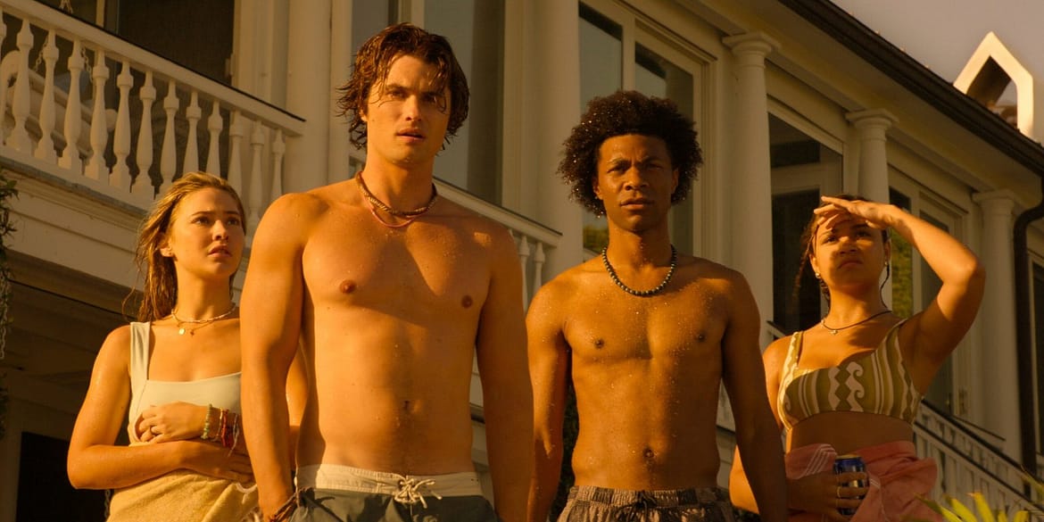 "Four young adults stand outside a large house in warm, golden sunlight. Two are shirtless, and the group looks intently ahead, suggesting curiosity or concern. The setting feels summery and relaxed."